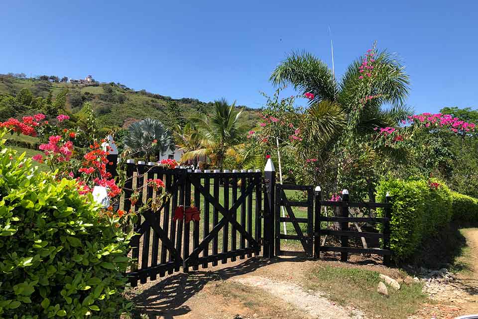 A closed gate on a dirt path, surrounded by greenery