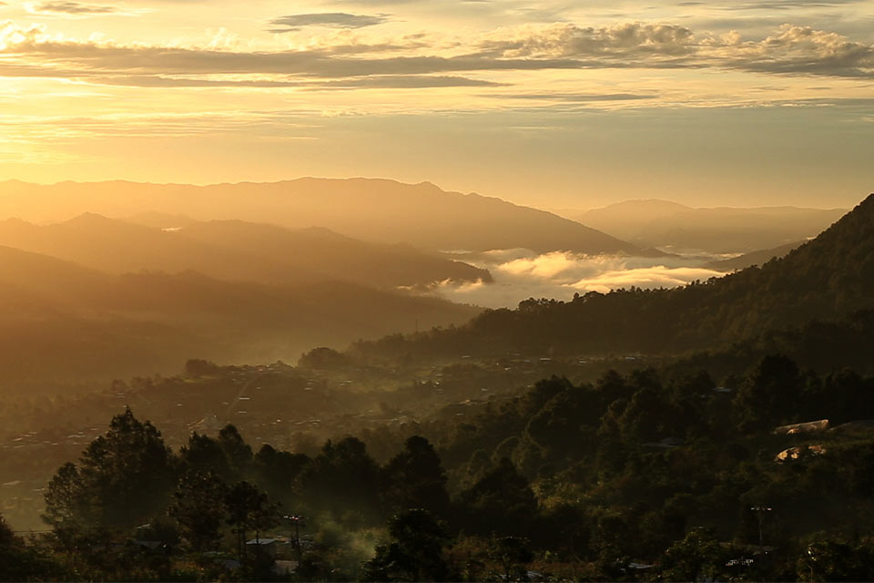 A photograph looking from up on high down at a river valley in the golden morning sun