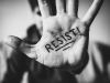 A black and white photograph of a hand with the word Resist written on the palm