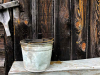 A photograph of an old galvanized steel bucket positioned in front of a wooden wall