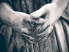 A somber black and white photo of the clasped hands of a statue, darkened by weathering