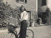 A black and white photo of Sylvia Plath with her bicycle smiling at the camera