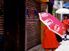 A woman, dressed in red, walks down the street, her face obscured by a red umbrella