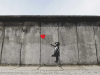 A painting of a girl in black and white holding a red balloon on a drab gray wall