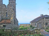 A rugged tower rises to the left of a stone house, both of which sit at the edge of the ocean