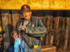 An older man in a hard hat and work coveralls appears as if he is speaking in a highly industrial location