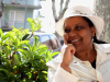 Ribka Sibhatu sits in a white suit and hat in front of a bush