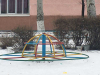 A photograph of a multi-colored merry go round on the snowy ground outside of a school