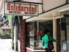 A photograph of a woman in a green jacket entering a book store. A sign above reads, “Solidaridad”