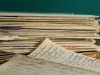 A photo of a stack of papers in front of a solid dark green background. A smaller stack sits in front where the handwritten letters are visible.