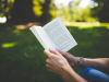 Person reading a book outside on green grass.