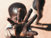 A photo of a young boy holding his hand up towards a camera, partially obscuring his own face