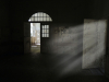 A photograph of a rundown room, mostly shrouded in shadow, with light streaking in an open door on the right