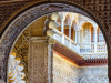 A photograph from inside of an archway that looks toward a balcony in the courtyard outside