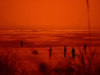 A photograph of figures on a beach. The photograph is heavily colored in red and orange tones.