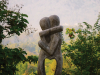 A photograph of a stone sculpture of two humanoid figures embracing. The status is in a jungle