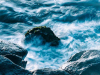 A photograph of a boulder jutting up from the churn of water flowing into an inlet