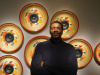 A man stasnds in front of a wall covered in decoratively painted mounted subwoofers 