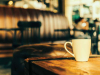 A photograph of a mug on a wooden table. A coffee shop can be seen out of focus in the background