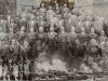 A collage composed of three photos. A black and white photograph of a group of black men dressed in suits. A photo of women similarly posed is overlain in the lower left hand corner and a photo of Tulsa burning overlain in the bottom right hand corner.