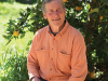 David Holmgren, sitting in the shade of a fruit tree, smiling at the photographer