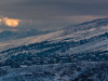 A photograph of a small village on a mountainside, shrouded in snow and shadow