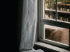 A rain laced window shot from inside a room draped in shade