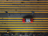 A shot from directly above of a red taxi cab waiting at a street light on a street marked by numerous parallel yellow lines