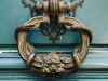 An ornate brass door knocker rests on a dark turquoise door