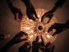 Looking up at a group of hands holding champagne glasses with a chandelier lighted but unfocused in the background.