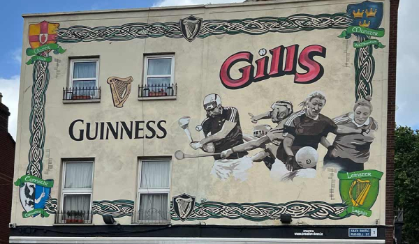 A mural on the side of a building. The mural shows sports figures and the text reads: Guiness. Gills.