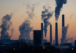 A photograph of an industrial park at dusk, smoke belching from tall stacks