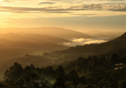 A photograph looking from up on high down at a river valley in the golden morning sun