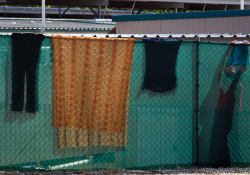 Clothes and other textiles hang on a chain-link fence surrounding tents