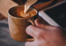 A photograph of someone pouring cream into coffee in a cup