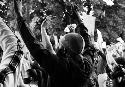 A black and white photo of a masked protestor with his hands up