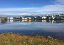 The city of Reykjavik framed in the foreground by a lake and in the background by cloud-capped mountains