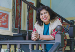 Dipika Mukherjee leans over a railing, smiling, as she looks at the camera