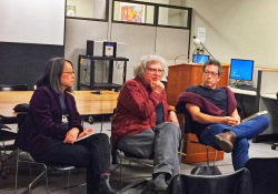 Three people sitting in chairs in conversation with an audience (which is off panel)