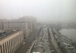 An aerial photograph of a crowded parking lot on a waterfront, shrouded in fog