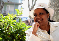 Ribka Sibhatu sits in a white suit and hat in front of a bush