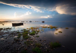 A boat floats in a desultory natural port as the sun begins to crest above the horizon