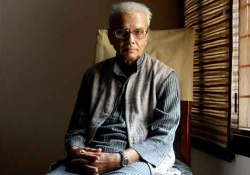 A photo of sitting looking at the camera with light coming in through the blinds to his right