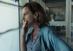 A photograph of a woman, her hand covering her mouth in a gesture of worry, stares out a window. 