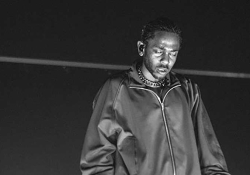 A black and white photo of Kendrick Lamar in performance, his eyes closed