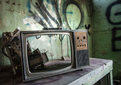 A photograph of a broken television with no screen in a room tagged with graffiti on the walls