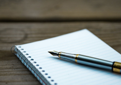 A fountain pen rests on a notebook of lined paper