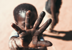 A photo of a young boy holding his hand up towards a camera, partially obscuring his own face