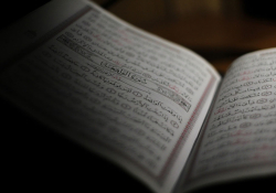 An open book written in Arabic, mostly shrouded in shadow