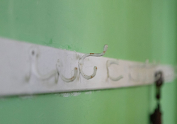 A photograph of a worn rack of coat hooks mounted on a white board, which is itself mounted on a lime-green wall